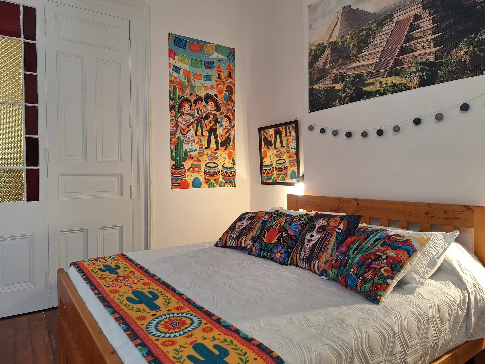 Cama con textiles y cuadros mexicanos en la habitación México de CasaFran